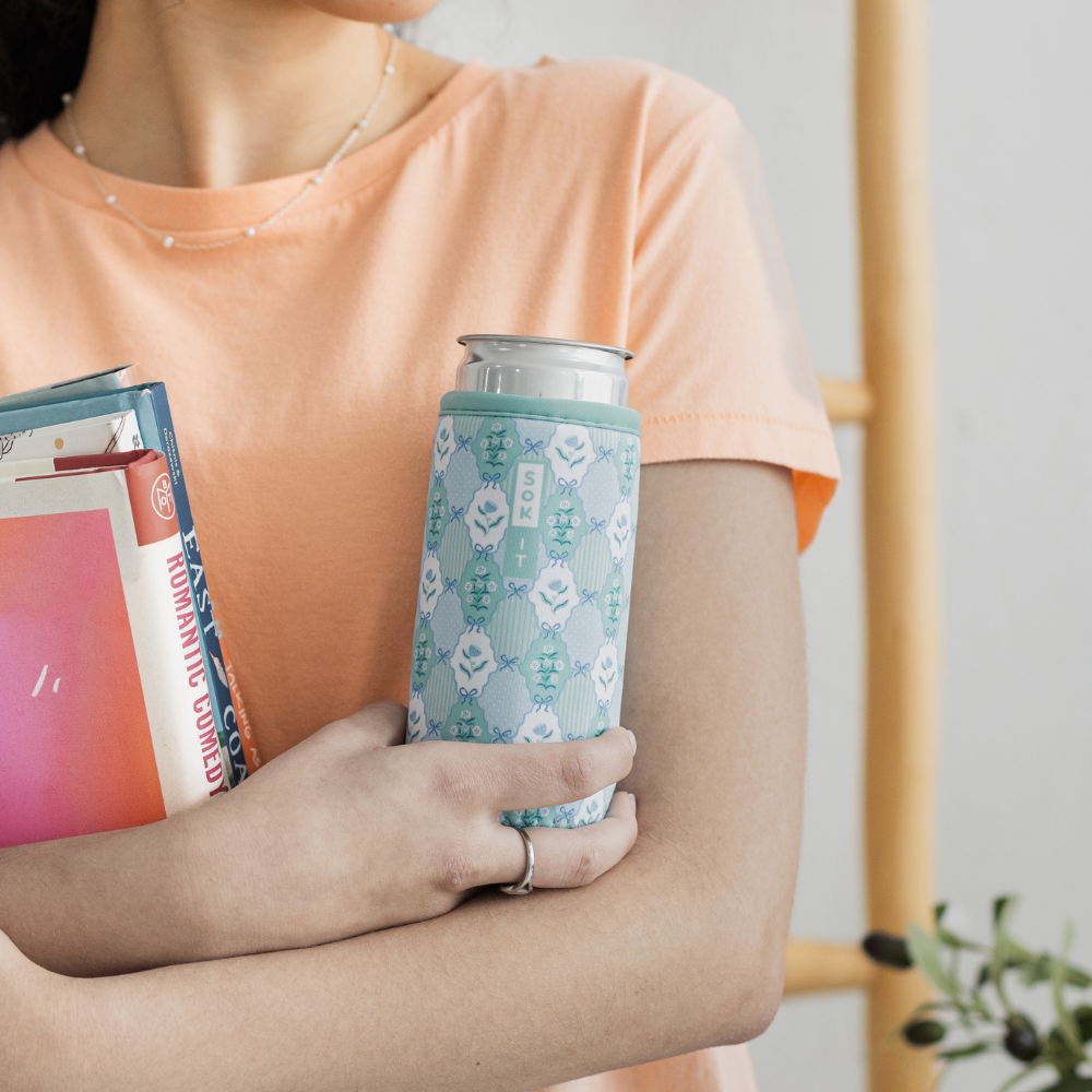 Person holding a can with a patterned sleeve and a book.
