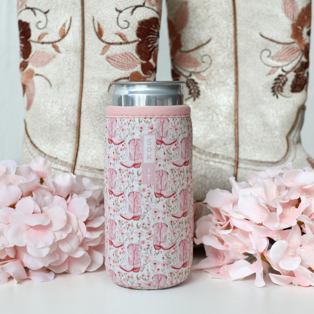 pink floral and cowgirl boot pattern can sleeve on silver skinny can with boots and flowers in the background