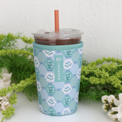 Tumbler with a patterned sleeve on a white surface with greenery in the background