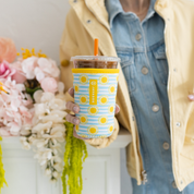 Person holding a iced coffee drink cup with a blue and white striped drink sleeve that has yellow subs all over it